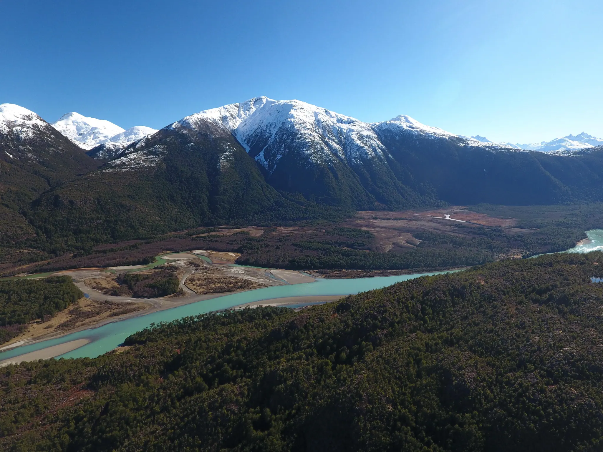 Río Baker de aguas turquesa bajo cerros nevados, con bosque nativo en primer plano