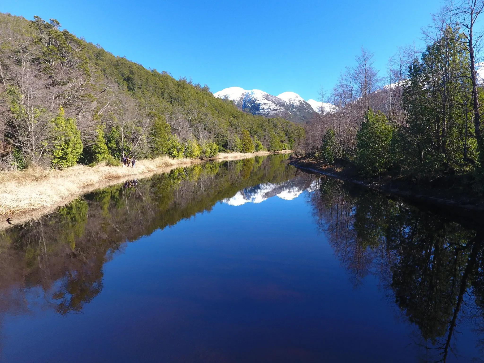 Aguas quietas del Río Vargas reflejando el bosque y las cumbres nevadas